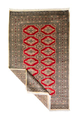 Alfombra Persa Yamouth beige y rojo de 1.20 x 1.97 mts, vista completa con una esquina doblada; el diseño muestra medallones romboidales rojos enlazados sobre un campo beige y guardas oscuras