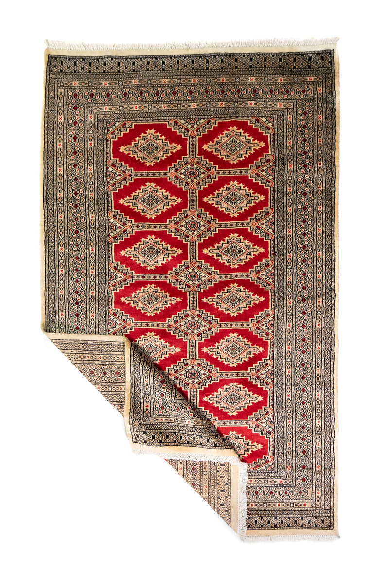 Alfombra Persa Yamouth beige y rojo de 1.20 x 1.97 mts, vista completa con una esquina doblada; el diseño muestra medallones romboidales rojos enlazados sobre un campo beige y guardas oscuras