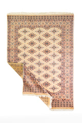 Alfombra Persa Yamouth beige de 1.27 x 1.78 mts, vista completa con una esquina doblada; el diseño muestra pequeños motivos romboidales repetidos sobre un campo beige y guardas cálidas