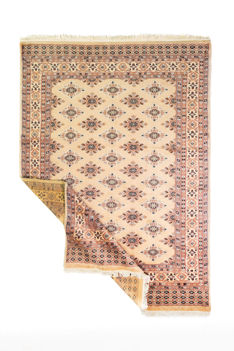 Alfombra Persa Yamouth beige de 1.27 x 1.78 mts, vista completa con una esquina doblada; el diseño muestra pequeños motivos romboidales repetidos sobre un campo beige y guardas cálidas