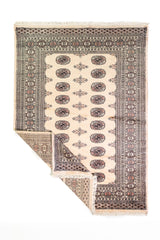 Alfombra Persa Bukara Yamouth beige de 1.37 x 1.83 mts, vista completa con una esquina doblada; el diseño muestra medallones ovalados oscuros sobre un campo beige con múltiples guardas geométricas