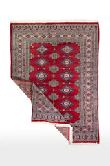 Alfombra Persa Yamouth rojo de 1.24 x 1.68 mts, vista completa con una esquina doblada; el diseño muestra medallones enlazados rojos sobre un campo claro con guardas geométricas azuladas
