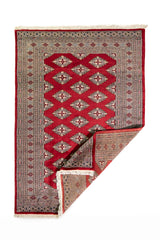 Alfombra Persa Yamouth rojo de 1.24 x 1.78 mts, vista completa con una esquina doblada; el diseño muestra una cadena de rombos rojos enlazados sobre un campo claro y guardas oscuras