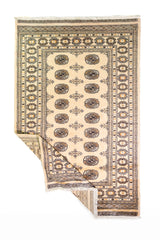 Alfombra Persa Bukara Yamouth beige de 1.27 x 1.86 mts, vista completa con una esquina doblada; el diseño muestra medallones ovalados oscuros sobre un campo beige y un marco geométrico bien definido