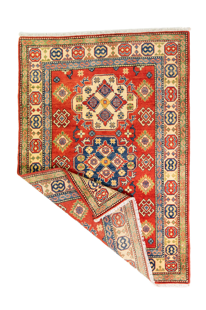 Alfombra Caucasica Kazak ladrillo con detalles multicolor de 1.24 x 1.78 mts, vista completa con una esquina doblada; el diseño muestra medallones y motivos geométricos de gran contraste distribuidos sobre un campo ladrillo con bordes multicolores