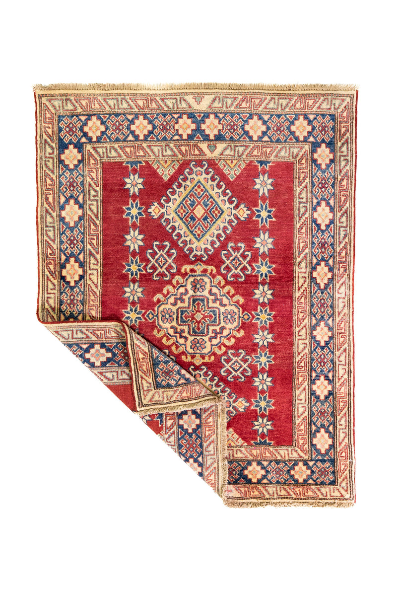 Alfombra Caucasica Kazak rojo y beige de 1.17 x 1.47 mts, vista completa con una esquina doblada; el diseño muestra medallones romboidales apilados sobre un campo rojo con amplias guardas beige