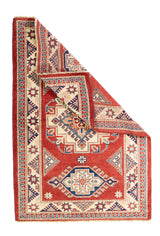 Alfombra Caucasica Kazak ladrillo y beige de 1.04 x 1.47 mts, vista completa con una esquina doblada; el diseño muestra tres medallones geométricos principales sobre un campo ladrillo con borde beige