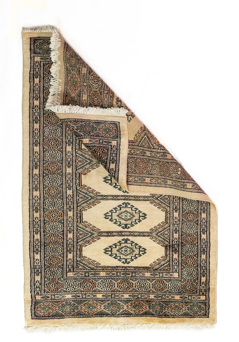 Alfombra Persa Yamouth verde y beige de 0.76 x 1.14 mts, vista completa con una esquina doblada; el diseño muestra una cadena central de grandes rombos beige sobre un campo verde oscuro con guardas geométricas