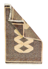 Alfombra Persa Yamouth gris y beige de 0.80 x 1.22 mts, vista completa con una esquina doblada; el diseño muestra grandes rombos beige enlazados sobre un campo gris oscuro con un marco geométrico estrecho