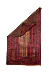Alfombra Persa Baluchistán Oración rojo y marrón de 0.85 x 1.45 mts, vista completa con una esquina doblada; el diseño muestra un campo rojo profundo con panel central estrecho y bandas geométricas repetidas de inspiración de oración