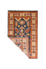 Alfombra Caucasica Kazak beige y azul de 0.83 x 1.30 mts, vista completa con una esquina doblada; el diseño muestra medallones geométricos azules sobre un campo beige con guardas de acento ladrillo