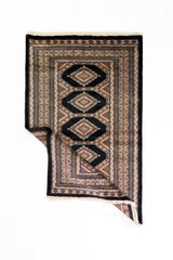 Alfombra Persa Bukara negro y gris de 1.52 x 0.94 mts, vista con una esquina doblada para mostrar guarda, reverso y estructura visual