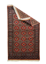 Alfombra Persa Bukara rojo de 0.92 x 1.55 mts, vista con una esquina doblada para mostrar guarda, reverso y estructura visual