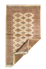 Alfombra Persa Bukara blanco y beige de 0.92 x 1.55 mts, vista con una esquina doblada para mostrar guarda, reverso y estructura visual