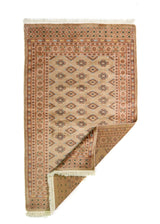 Alfombra Persa Bukara marrón de 0.99 x 1.60 mts, vista con una esquina doblada para mostrar guarda, reverso y estructura visual