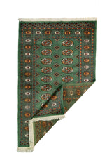 Alfombra Persa Bukara verde oscuro de 0.97 x 1.55 mts, vista con una esquina doblada para mostrar guarda, reverso y estructura visual