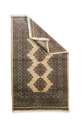 Alfombra Persa Bukara beige y gris de 0.95 x 1.55 mts, vista con una esquina doblada para mostrar guarda, reverso y estructura visual