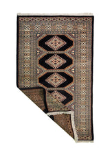 Alfombra Persa Bukara negro y beige de 0.94 x 1.52 mts, vista con una esquina doblada para mostrar guarda, reverso y estructura visual