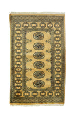 Alfombra Persa Bukara mostaza y beige de 0.76 x 1.27 mts, vista completa de la pieza con medallones ovalados repetidos sobre un campo mostaza, acompañados por guardas oscuras