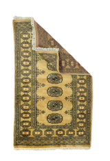 Alfombra Persa Bukara mostaza y beige de 0.76 x 1.27 mts, vista con una esquina doblada para mostrar guarda, reverso y estructura visual