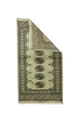Alfombra Persa Bukara verde y negro de 0.59 x 1.24 mts, vista con una esquina doblada para mostrar guarda, reverso y estructura visual