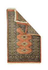 Alfombra Persa Bukara marrón y gris de 0.92 x 1.42 mts, vista con una esquina doblada para mostrar guarda, reverso y estructura visual