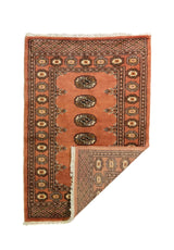 Alfombra Persa Bukara marrón de 0.81 x 1.22 mts, vista con una esquina doblada para mostrar guarda, reverso y estructura visual