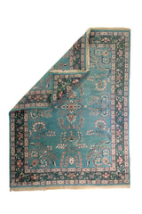 Alfombra Persa Nain verde y celeste de 2.35 x 3.00 mts, vista completa con una esquina doblada; se observan motivos florales y vegetales continuos con guarda ornamental