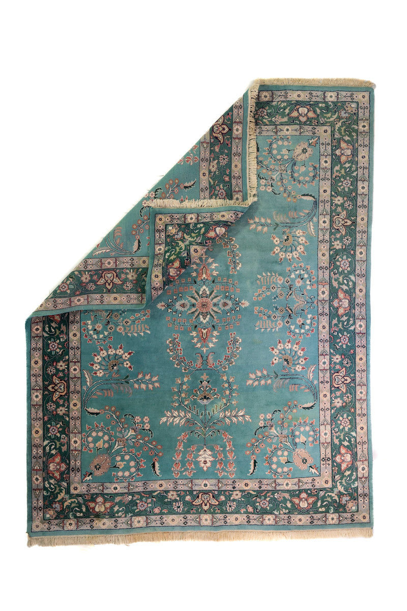Alfombra Persa Nain verde y celeste de 2.35 x 3.00 mts, vista completa con una esquina doblada; se observan motivos florales y vegetales continuos con guarda ornamental