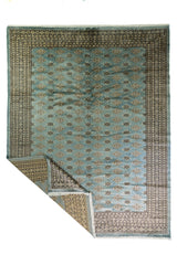Alfombra Persa Bukara celeste de 2.52 x 3.61 mts, vista completa con una esquina doblada y guardas visibles; se observan motivos geométricos pequeños repetidos y guardas contrastantes