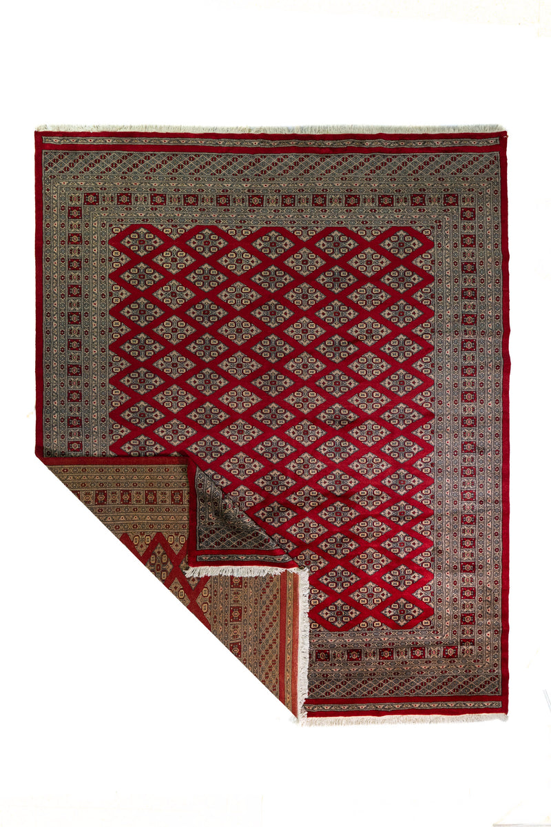 Alfombra Persa Bukara Yamouth rojo de 2.49 x 3.07 mts, vista completa con una esquina doblada; se observan entramado de rombos y guardas geométricas de alto contraste