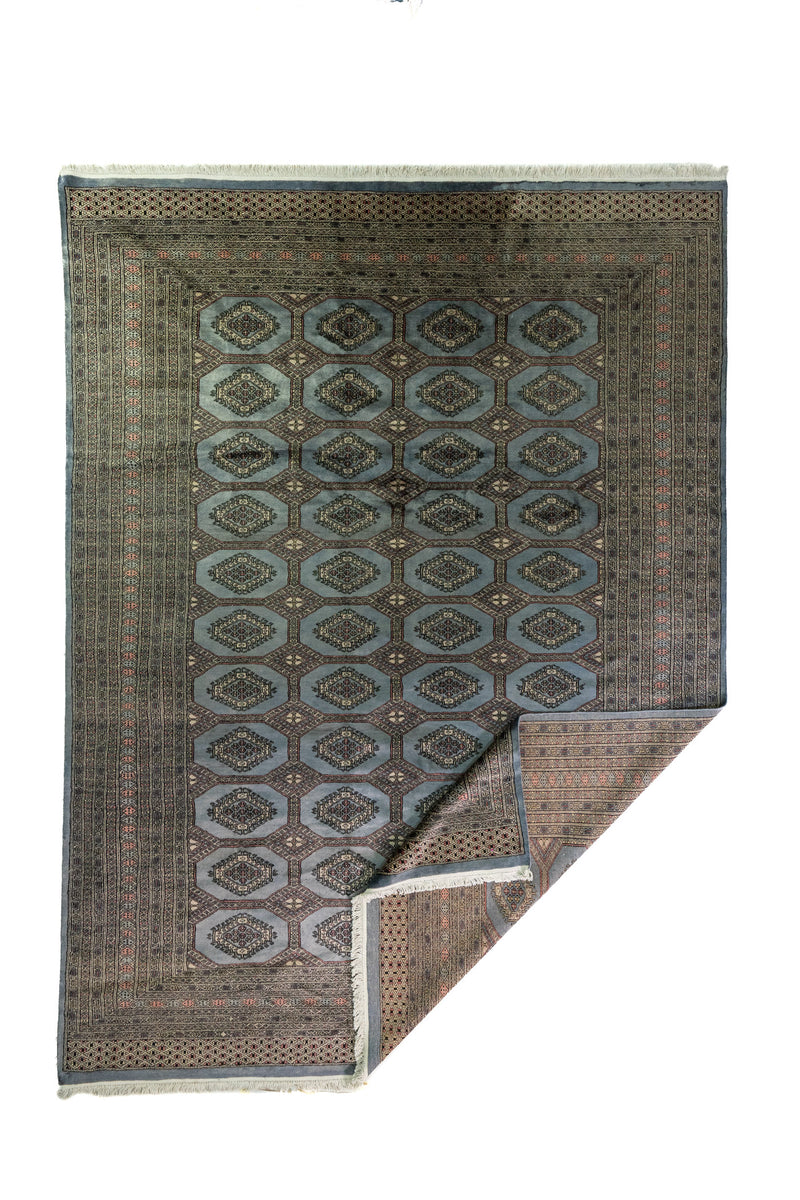 Alfombra Persa Bukara Yamouth celeste de 2.48 x 3.38 mts, vista completa con una esquina doblada; se observan medallones geométricos repetidos y guardas definidas