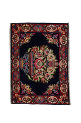 Alfombra Persa Sarouk azul y rojo de 0.69 x 1.05 mts, vista completa de la pieza con un medallón floral central sobre un campo azul oscuro, rodeado por una guarda roja de motivos vegetales