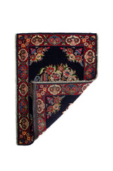 Alfombra Persa Sarouk azul y rojo de 0.69 x 1.05 mts, vista con una esquina doblada para mostrar guarda, reverso y estructura visual