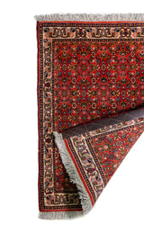 Alfombra Persa Horazan rojo y beige de 0.48 x 0.69 mts, vista con una esquina doblada para mostrar guarda, reverso y estructura visual