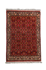 Alfombra Persa Horazan rojo y beige de 0.48 x 0.69 mts, vista completa de la pieza con pequeños motivos repetidos sobre un campo rojo, acompañados por guardas beige de inspiración tradicional