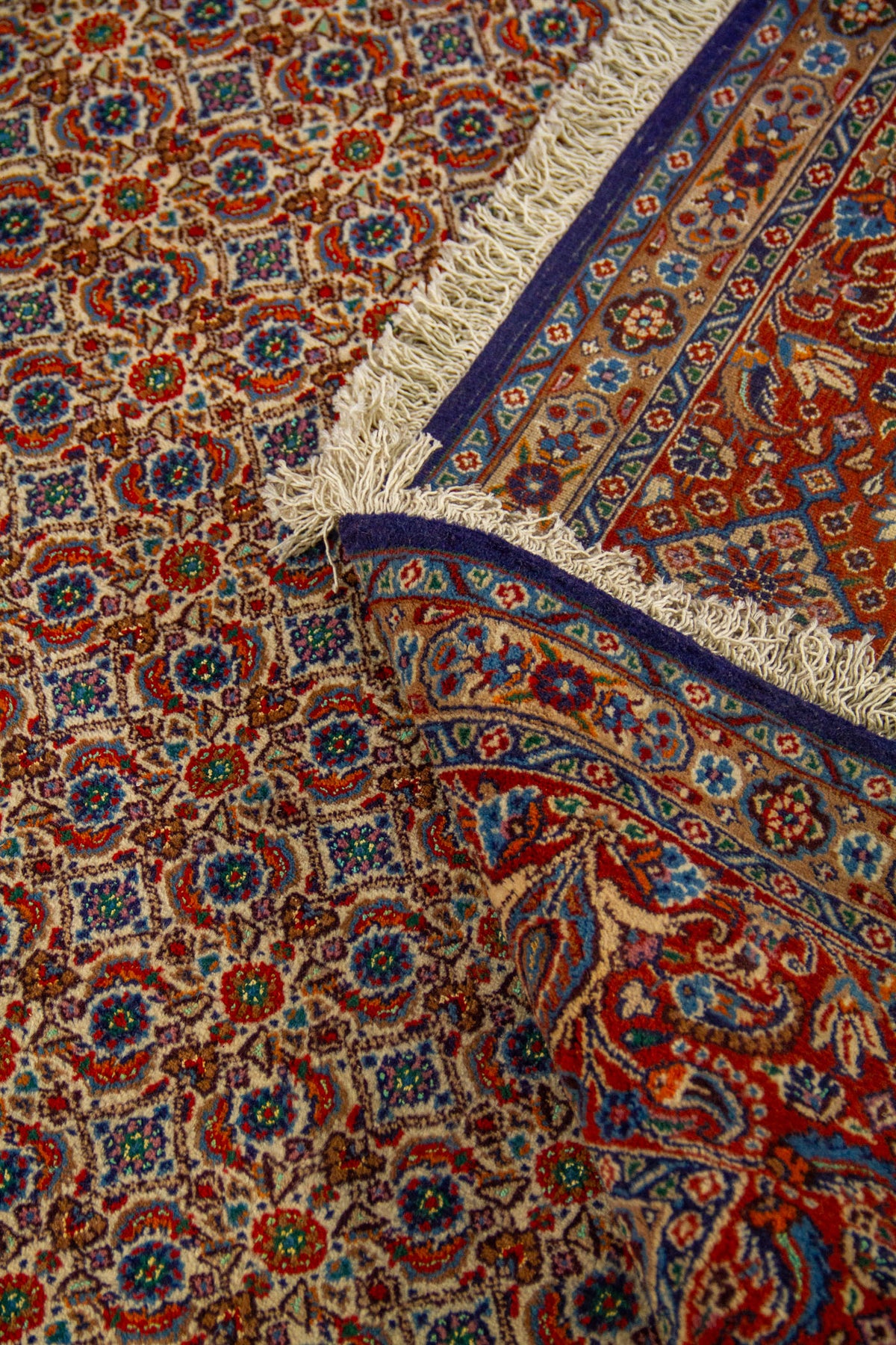 Alfombra doblada mostrando la densidad del diseño repetitivo, el detalle de la guarda y el acabado con flecos.