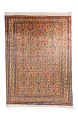 Alfombra clásica de inspiración oriental con fondo anaranjado claro, diseño repetitivo de motivos florales  y guardas decorativas en tonos beige, azul y rojo.