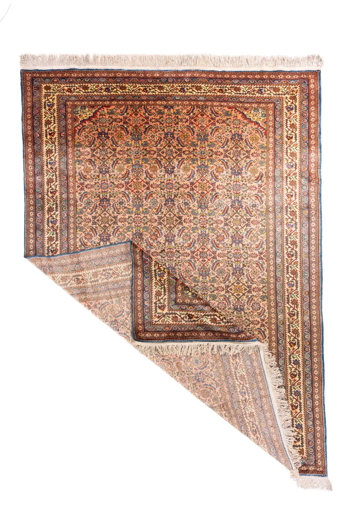 Alfombra oriental tradicional con una esquina doblada que permite ver el reverso, la estructura del tejido y los flecos en tono blanco suave.