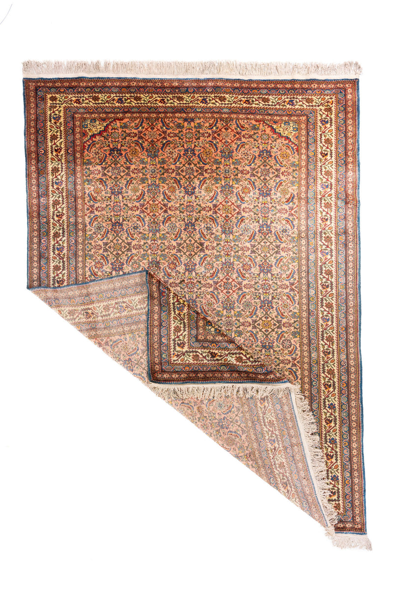 Alfombra oriental tradicional con una esquina doblada que permite ver el reverso, la estructura del tejido y los flecos en tono blanco suave.