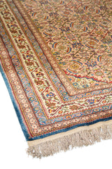 Vista en ángulo de alfombra clásica con diseño floral repetitivo, guardas múltiples decoradas y combinación de tonos anaranjado claro, azul, beige y rojo.