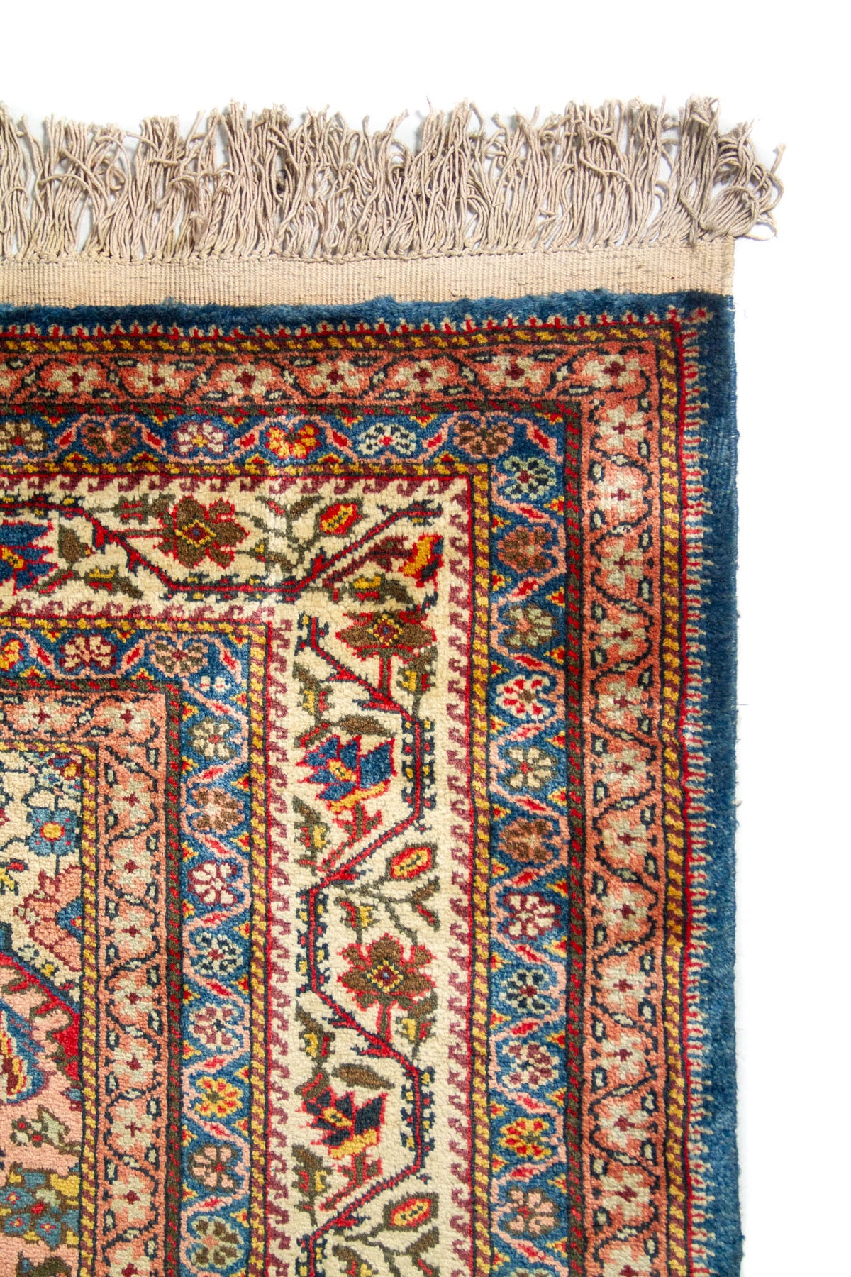 Primer plano de la esquina superior de una alfombra oriental con bordes detallados, flecos claros y patrones florales tradicionales.