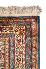 Primer plano de la esquina superior de una alfombra oriental con bordes detallados, flecos claros y patrones florales tradicionales.