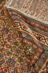 Detalle de alfombra doblada mostrando el reverso, los flecos y la riqueza del diseño ornamental en tonos suaves y elegantes.