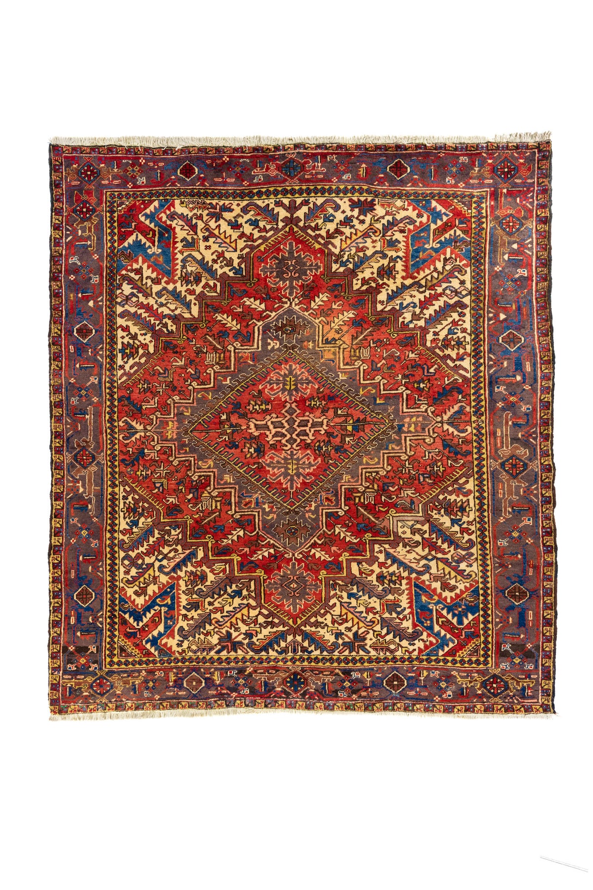 Alfombra estilo tribal con gran medallón geométrico rojo, fondo beige y guarda azul con motivos en rojo y dorado.