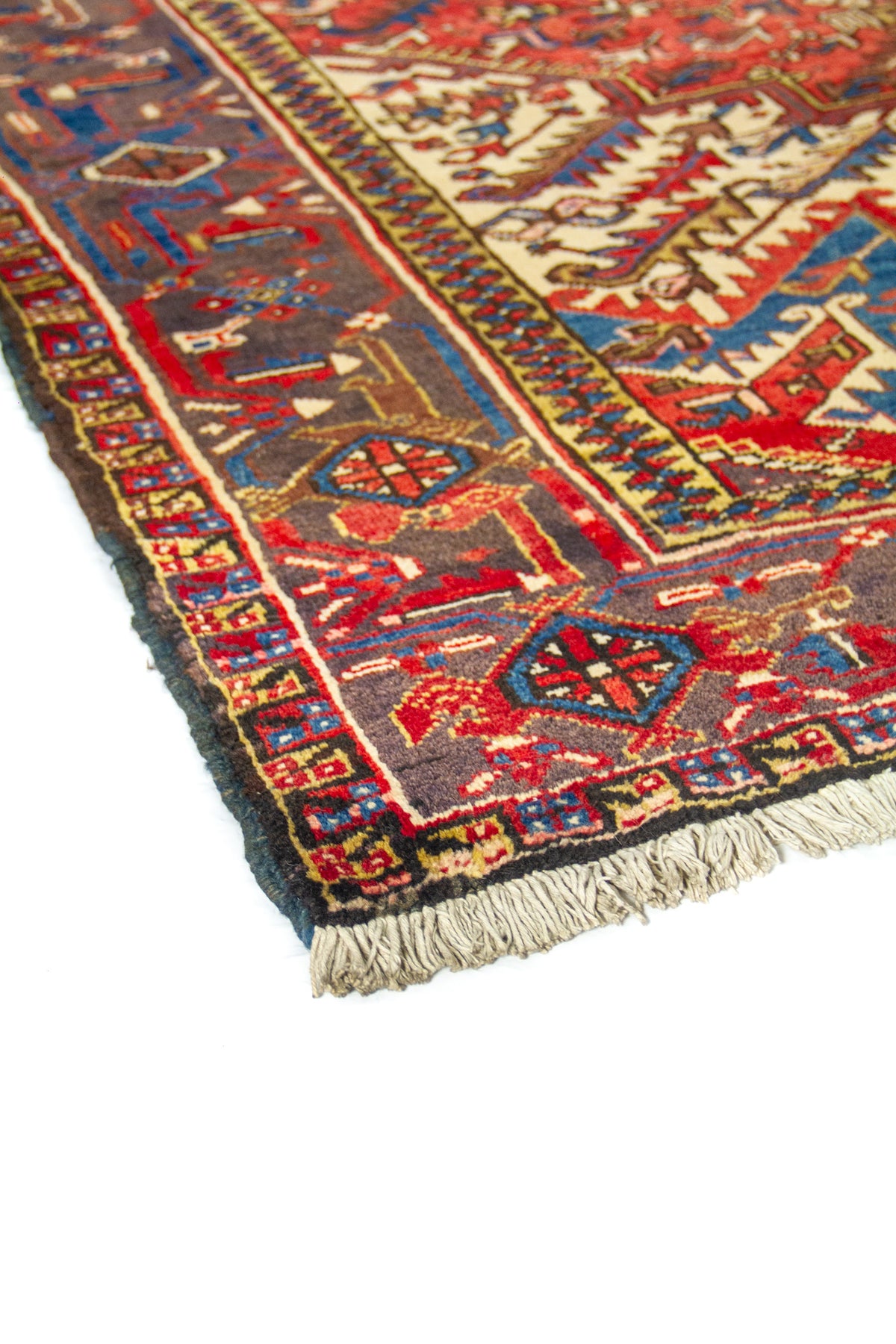 Vista en perspectiva de la alfombra con borde azul y campo central rojo; se aprecian flecos y relieve del tejido.