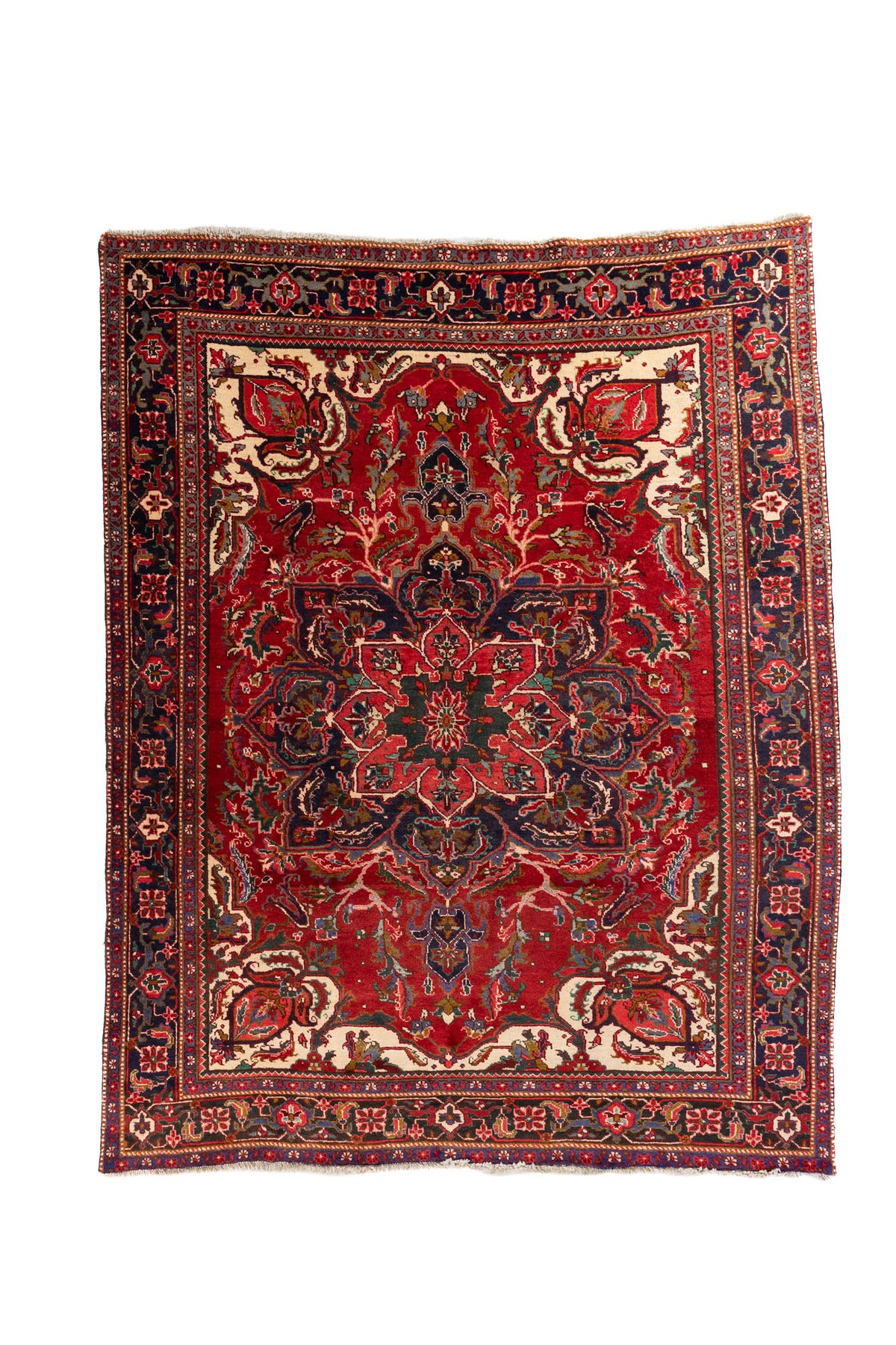 Alfombra oriental de fondo rojo intenso con gran medallón central, detalles marfil y guarda azul oscuro con motivos geométricos.