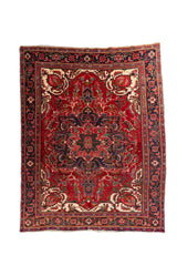 Alfombra oriental de fondo rojo intenso con gran medallón central, detalles marfil y guarda azul oscuro con motivos geométricos.
