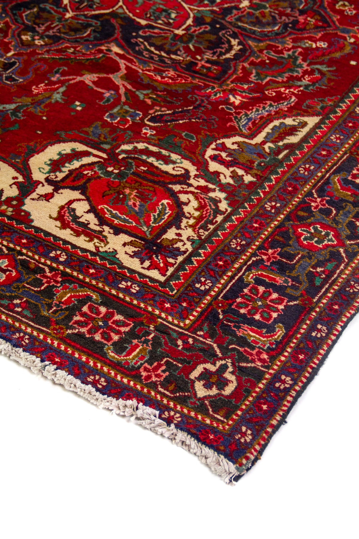 Detalle en perspectiva de alfombra roja con diseño central ornamental, marco azul oscuro y terminación con flecos claros.