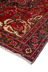 Detalle en perspectiva de alfombra roja con diseño central ornamental, marco azul oscuro y terminación con flecos claros.